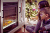 Girl and boy sitting comfortably in front of an electric fire, basking in its warm glow